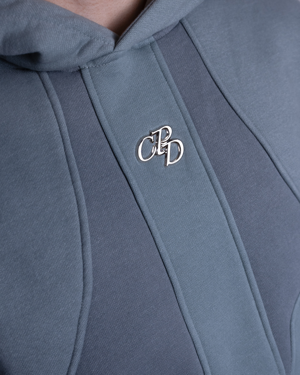 Grauer Tracksuit von COMME PAS DE DEUX mit metallischem Patch, Nahaufnahme des Details auf Stoff.